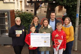 Bürgermeister Sacha Reichelt und Melanie Barth stehen gemeinsam mit Erwachsenen und Kindern aus Horrheim und einem Scheck über 1300 Euro auf dem Luisenplätzchen. 