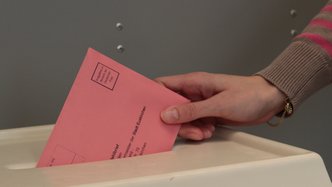 Jemand wirft einen Wahlzettel in die Urne. 