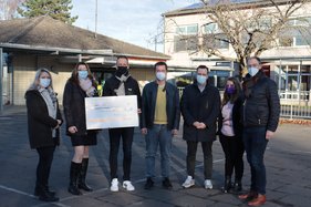Eine Menschengruppe auf dem Schulhof in Kuchenheim mit einem symbolischen Scheck.