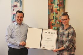 Euskirchens Bürgermeister und eine Mitarbeiterin zeigen eine Urkunde in die Kamera.